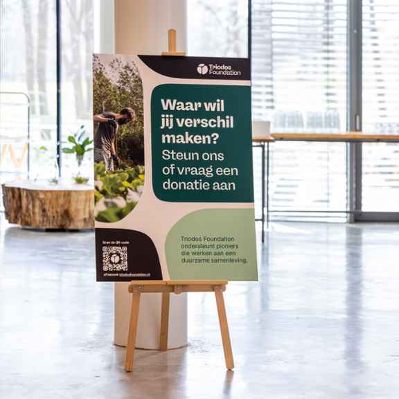 Een bord met de tekst "Waar wil jij verschil maken? Steun ons of vraag een donatie aan" van Triodos Foundation.