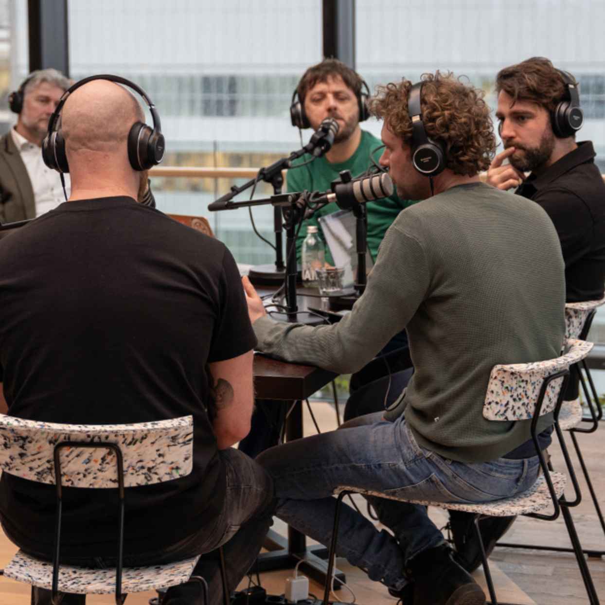 Mannen zitten met koptelefoons en microfoons aan tafel tijdens de opname van een podcast.