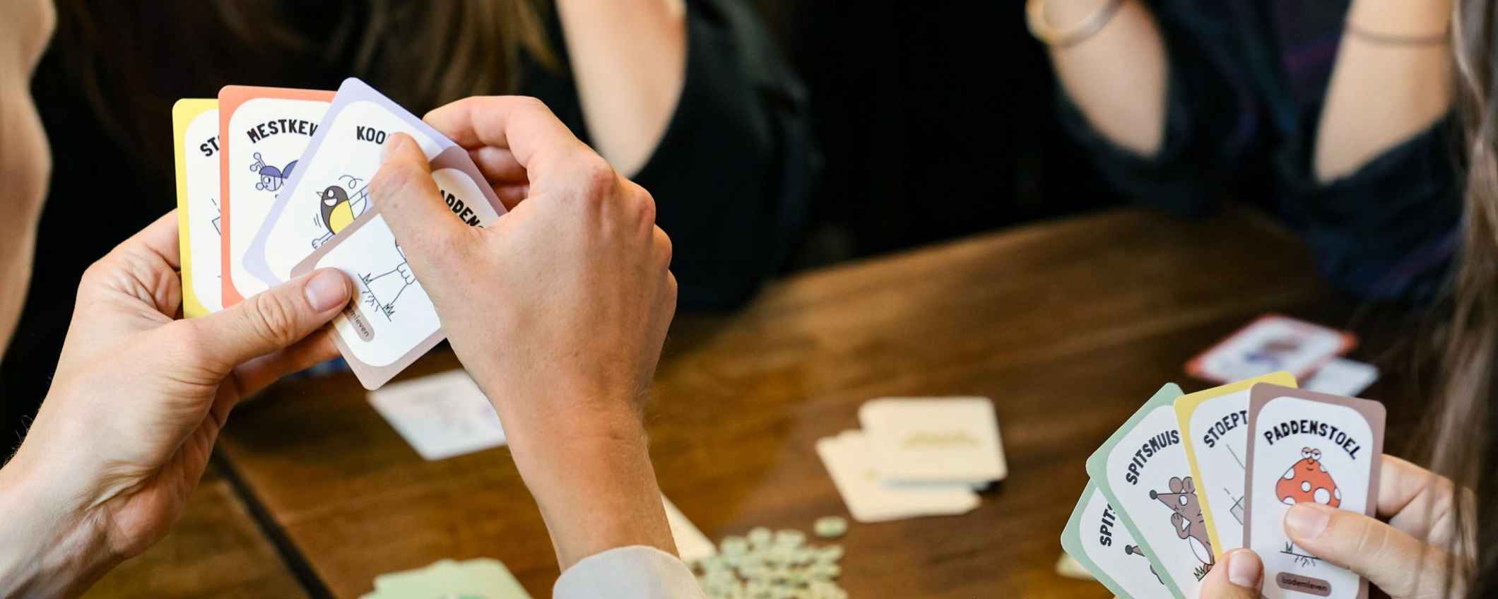 Close-up van het Plantje Boom spel en handen van mensen die ermee spelen aan een koffietafel.