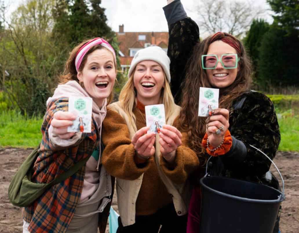 3 dames houden een bloemzaadzakje vast en lachen naar de camera.